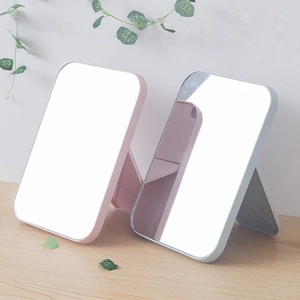 Minimalist portable folding vanity mirror in pink and blue on a wooden desktop