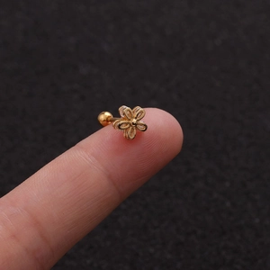 Macro shot of tiny gold flower stud earring with white zircon on a fingertip