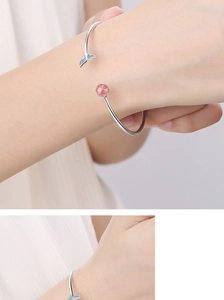 Detail of silver fish tail bracelet with red strawberry quartz bead on a wrist
