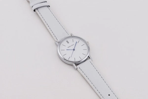 Detailed view of minimalistic silver watch face with blue hands and white leather strap