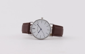 Detail of minimalist quartz watch with brown leather strap and silver round case