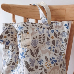Close-up of canvas tote bag with blue flowers and forest deer patterns on a wooden chair