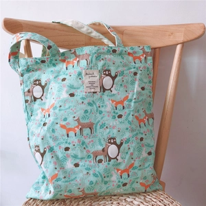 Close-up of mint green canvas tote bag with cute forest animals and beige woven label