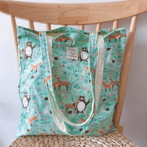 Detail of mint green floral canvas tote bag featuring forest animal patterns on wooden chair