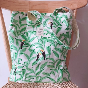 Detail view of cotton tote bag featuring tropical leaf prints and a black hornbill bird