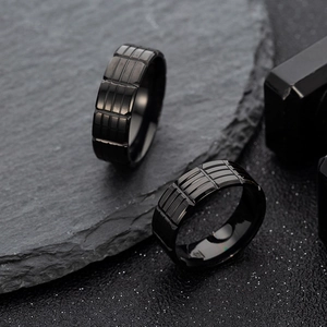 Detailed close-up of two black stainless steel rings with industrial groove patterns on rock