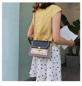 Detail of a chic color-block handbag with gold hardware and chain strap on a model