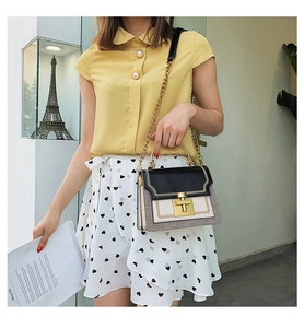 Fashionable black and beige shoulder bag with gold metal handle on model in indoor setting