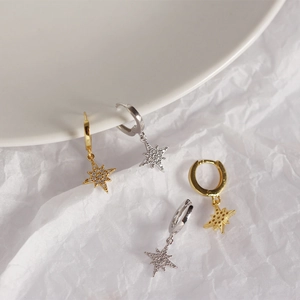 Close-up of gold and silver S925 star drop earrings with cubic zirconia on white paper