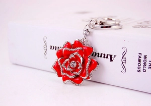 Detailed view of silver metal keychain with rhinestone-edged red rose on a white book