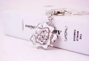 Close-up of a white enamel rose keychain with sparkling rhinestones on a metal floral charm