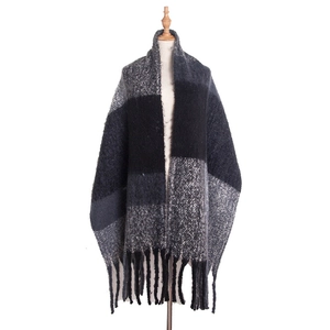 Detail of knit poncho wrap showing black and white plaid pattern and tassel fringe finish