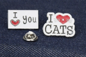 Close-up of I Love You and I Love Cats enamel pins on blue denim fabric background