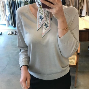 Gros plan d'un pull en maille gris clair à col en V avec un foulard en soie à motifs