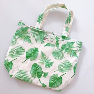 Detailed view of white cotton tote bag featuring green tropical leaf prints and zipper closure