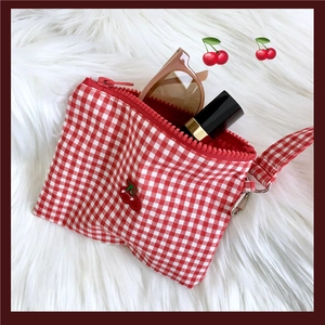 Detail der rot-weiß karierten Kosmetiktasche mit Kirschstickerei und Make-up