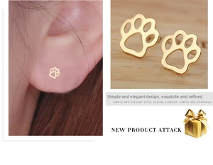 Close-up of minimalist rose gold paw print stud earrings worn by a model with wood background