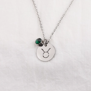 Detail of silver Taurus zodiac necklace with a round green birthstone pendant on fabric