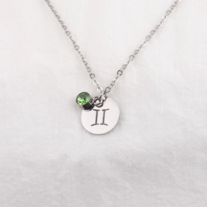 Macro shot of silver stainless steel zodiac necklace with green gemstone and roman numeral II