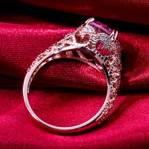 Rose gold engagement ring with pink gemstone and lace filigree on red silk background
