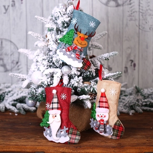 Three linen Christmas stockings with reindeer, Santa, and snowman hanging on a festive tree