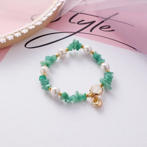 Detail of beaded bracelet with green stones, pearls and golden shell charm on soft lace