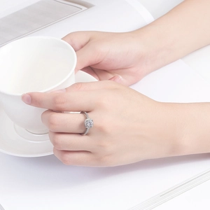 Close-up of a square-cut diamond ring with side stones on a finger by a coffee cup