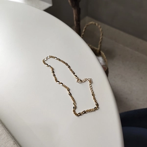 Detailed view of the gold double-layered link chain anklet on a white surface