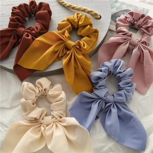 Detail of five Morandi color chiffon bow scrunchies on rustic props and white fabric