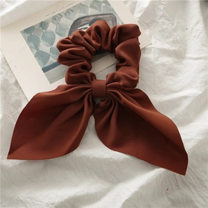 Detail of caramel bow scrunchie with soft fabric texture on a white textile surface