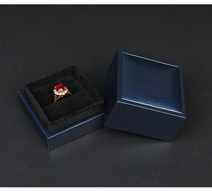 Macro shot of navy blue jewelry box with brushed texture and gold ruby ring inside