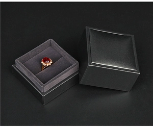 Detail of a black lid-and-base jewelry box with gray velvet lining and a gold gemstone ring