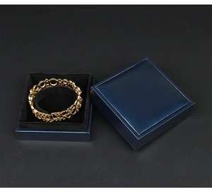 Close-up of a gold round pattern bracelet inside a deep blue jewelry box with black velvet