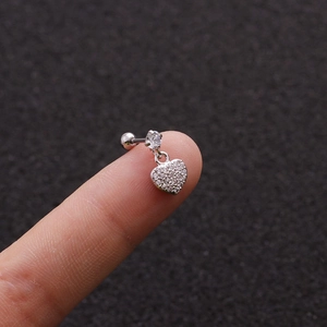 Macro shot of small heart dangle earring with tiny zircons held on fingertip