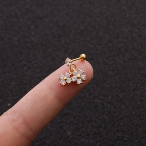 Macro shot of gold floral stud earrings with clear zircons held on a fingertip
