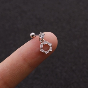 Macro shot of a small silver stud earring with hexagonal zircon pendant held on a fingertip