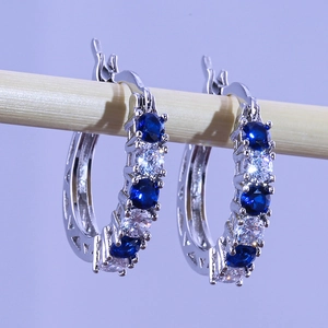 Silver hoop earrings with blue and clear zircon stones on a wooden display stand