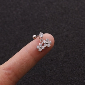 Macro shot of silver flower ear piercings with cubic zirconia held on a fingertip