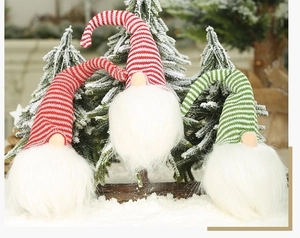 Trois gnomes de Noël en peluche avec bonnets rayés accrochés à des branches de sapin enneigées