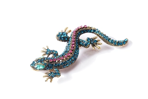 Detailed close-up of crystal lizard brooch with blue and pink rhinestones on gold base