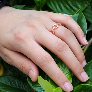 Rose gold chain link ring with pavé-set zircons displayed on finger with leaf background
