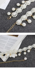 Detail of beaded pearl belt with gold lobster clasp and adjustable chain on grey fabric