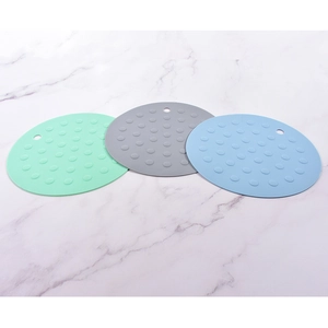 Three circular silicone placemats in green grey and blue with raised dots on marble surface