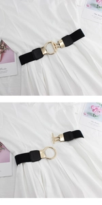 Détail d'une ceinture élastique noire avec boucle ronde dorée sur une robe blanche