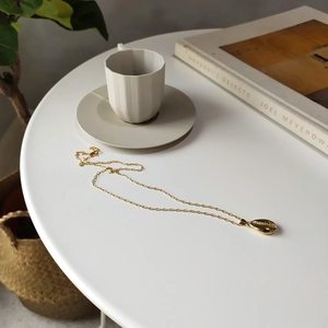 Artistic close-up of a gold seashell pendant necklace on a minimalist white table