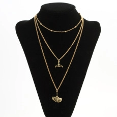 Close-up of golden layered necklace with whale tail and ginkgo leaf charms