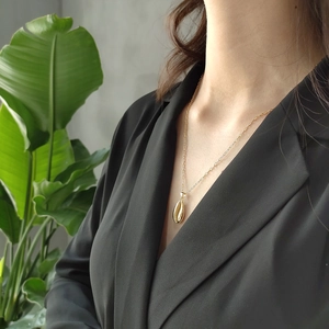 Close-up of a gold shell pendant necklace worn by a model against a green leaf background