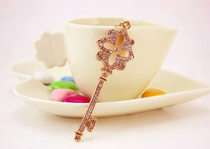 Close-up of a gold four-leaf clover key pendant with sparkling rhinestones on a white cup