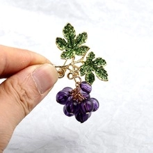 Detail of elegant grape-shaped brooch with purple beads, green leaves and gold finish