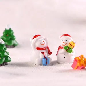 Miniature Christmas snowman figurines with gift boxes on white snow landscape